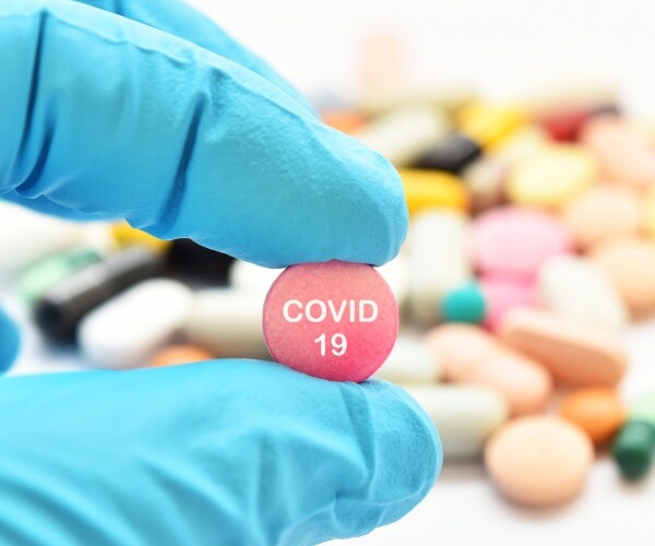 hand holding a pill that says "COVID-19" on it