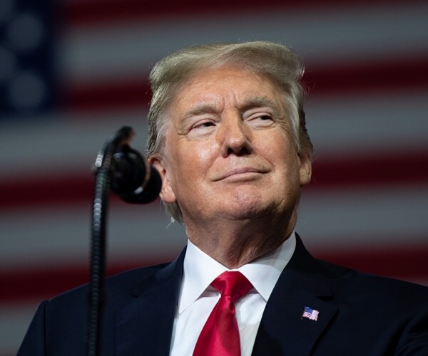 donald trump smiles at a mic in front of a flag