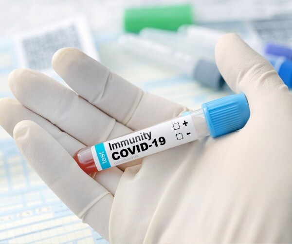 a hand with surgical glove holding a vial labeled "COVID-19 immunity"