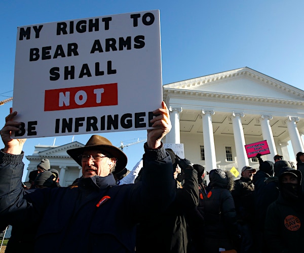 a man holds a sign in front of the Virginia State Capitol