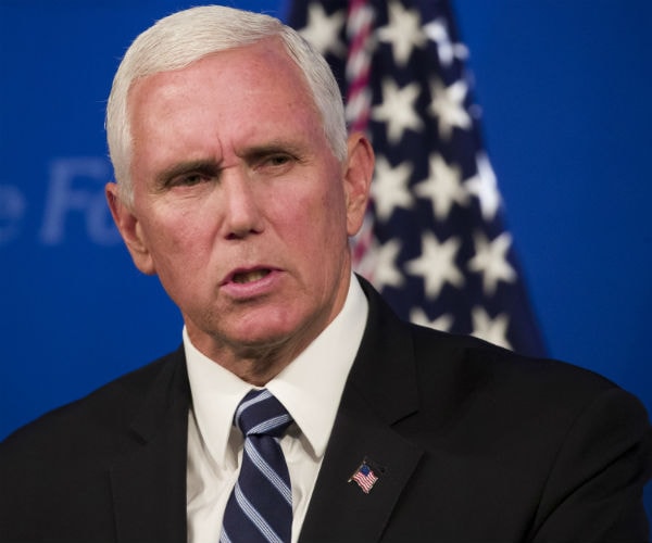 vice president mike pence is shown in a black suite with the american flag in the background and on his lapel