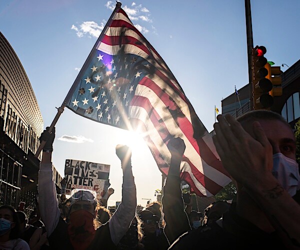 a black lives matter protester holds up the american flag upside down