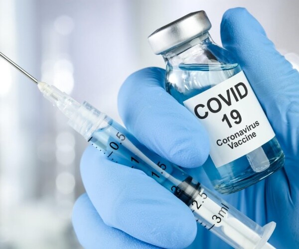 gloved hand holding COVID vaccine vial and syringe