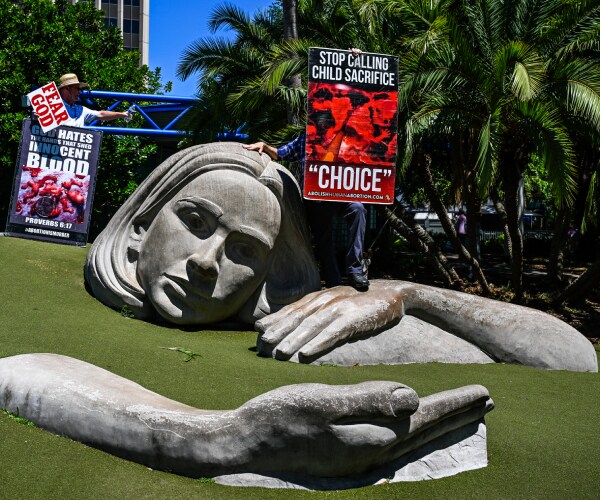 people hold signs near a statue of a woman