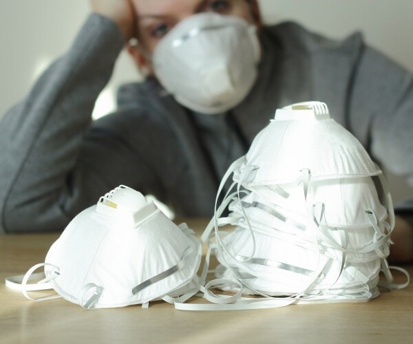 person with a mask on sitting in front of a pile of masks stacked on each other