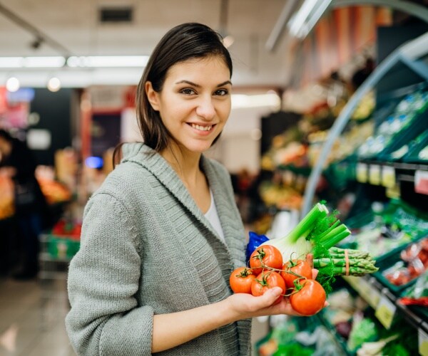 woman in grocery store holding vegetables and smiling at camera