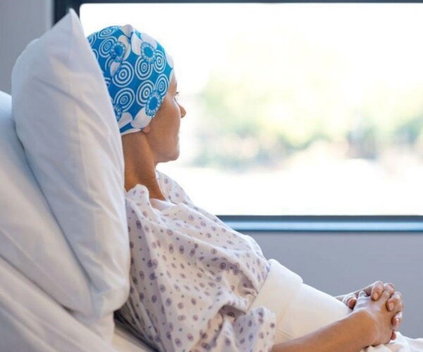 woman in hospital bed with scarf on head looking out window