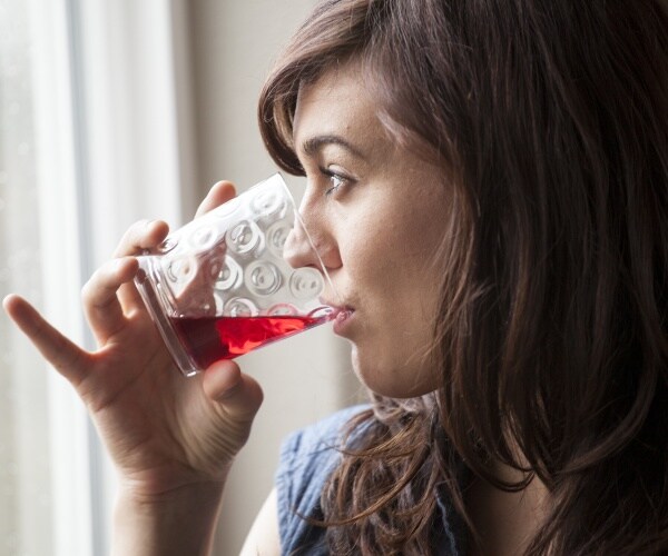 woman drinking a glass of cranberry juice as she looks out window