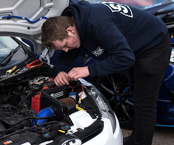 a man bends over an puts his head under the hood of a car for maintenance