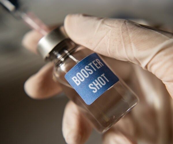 close-up of vial labeled "COVID booster" with syringe in it