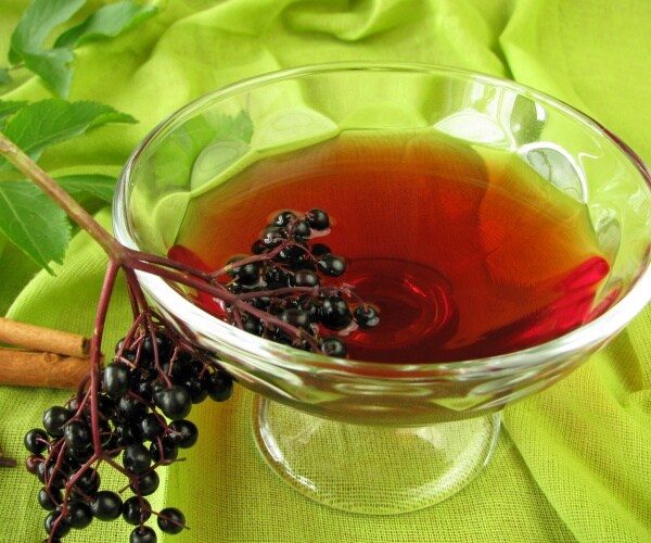 a glass with elderberry juice and some elderberries on the side