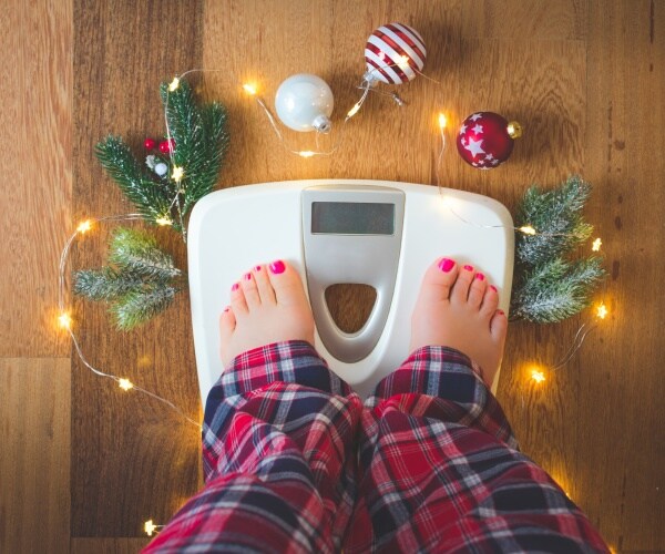 woman weighing herself on scale with holiday decorations around on floor