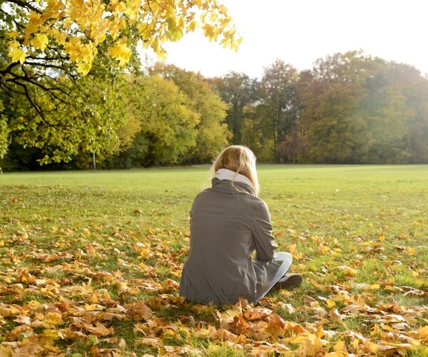 woman sitting by herself on grass in park in fall