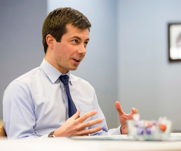 mayor pete buttigieg gestures with his hands while speaking during an interview while sitting at a desk