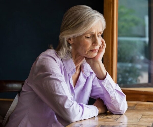 older woman sitting at table looking sad, depressed