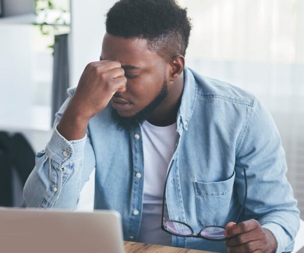 man looking at computer, holding top of nose because feeling brain fog