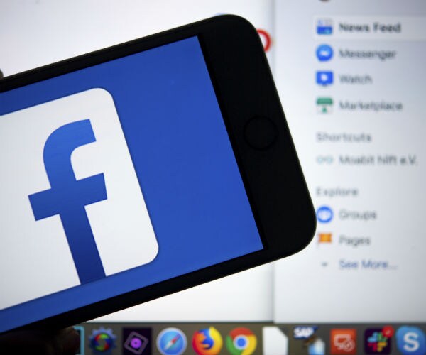 the facebook logo is seen on a cell device with a computer in the background