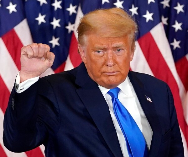 Trump pumping his fist on election night wearing a suit and blue tie with us flags behind him