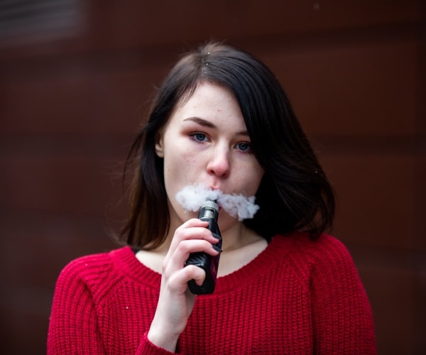 close-up of teenage girl vaping and looking at camera