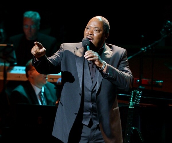 clayton in a suit performing on stage and singing into a mic