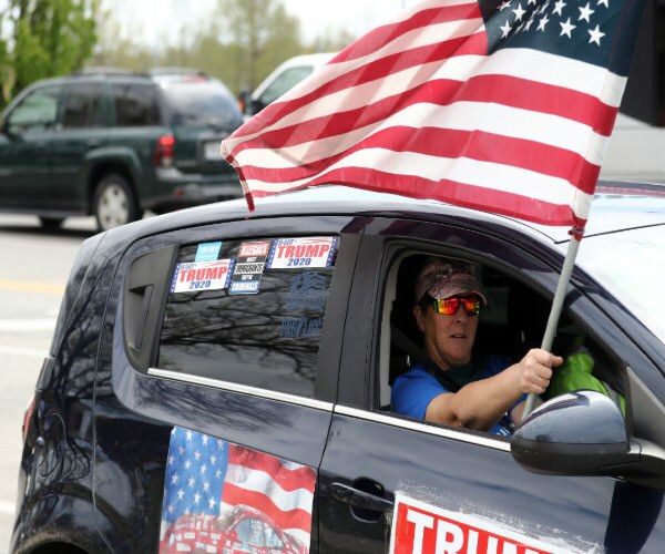 a trump supporter waves an american flag from inside a car to protest shutdowns in missouri