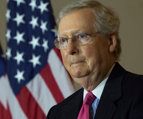 mitch mcconnell stands in front of flags