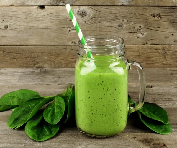 spinach smoothie in glass mason jar mug, with spinach leaves on wood table