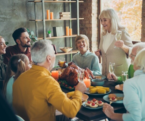 family crowded around Thanksgiving table, grandmother saying a toast