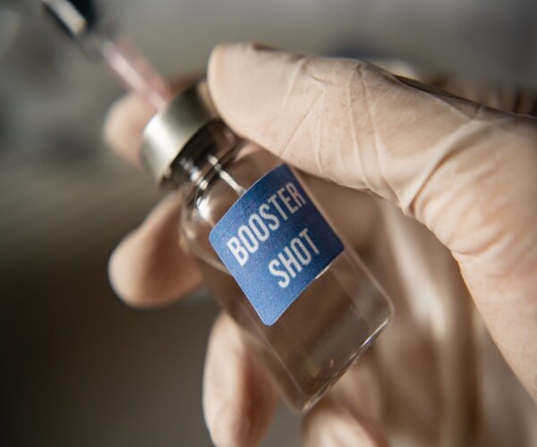 a gloved hand holding a vial labeled "booster shot"