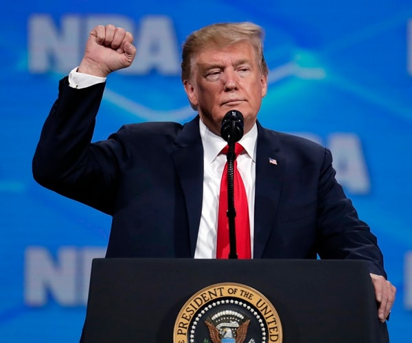 president trump holds up a fist on a stage supporting the nra