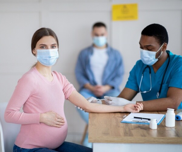 Pregnant woman in mask looking at camera while getting COVID vaccine