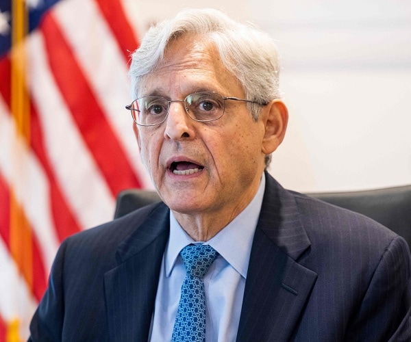 merrick garland sits at table in front of american flag