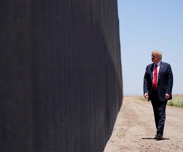 donald trump stands next to border wall