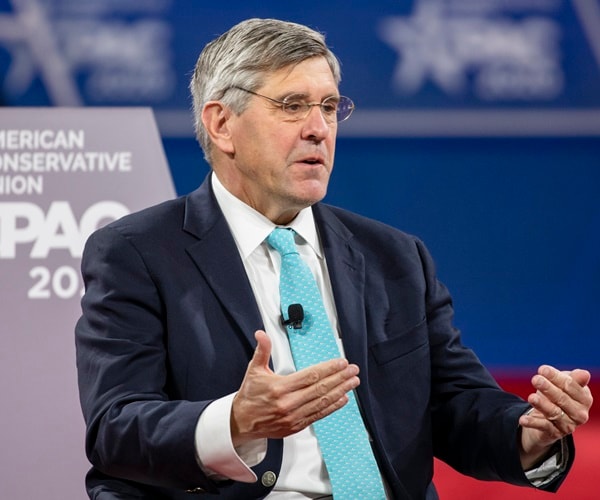 stephen moore sits in front of a cpac sign and speaks