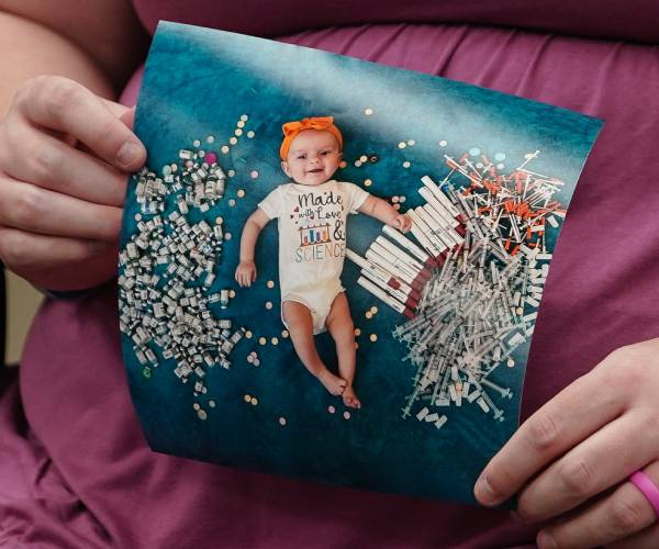 a woman holds a photo of a baby wearing a onesie that says made with love & science