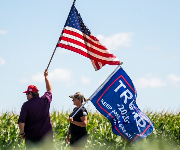 trump supporters wave a trump 2020 flag and an american flag in a field